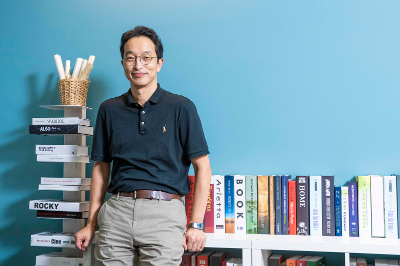 씨메스 이성호 대표가 파란 벽 앞 책장 옆에 서서 미소 짓고 있다