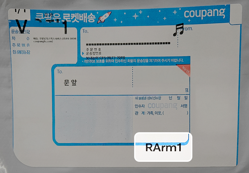 문 앞으로 배송 요청된 쿠팡 로켓배송 포장지. 상단에는 쿠팡 로켓배송 문구와 로켓 일러스트가 있으며, 수령자 서명란과 주문번호/운송장 번호 입력란이 포함되어 있음. 하단 오른쪽에는 ‘RArm1’ 코드가 기재됨.