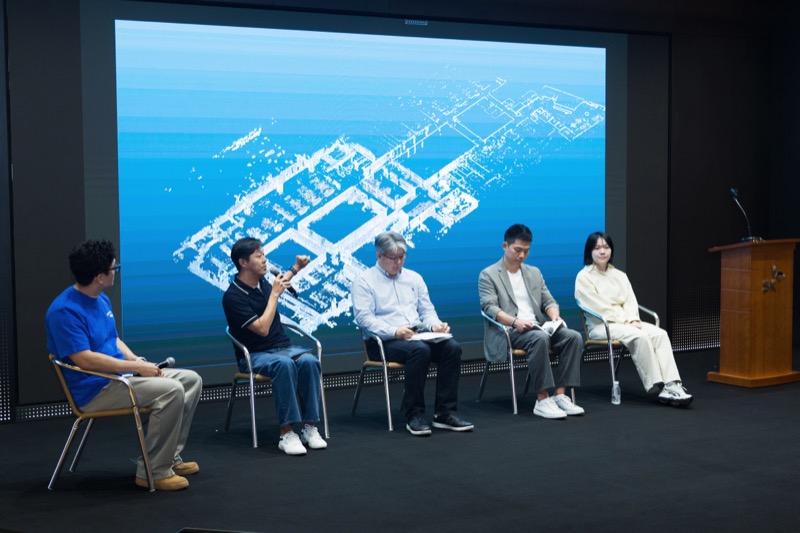 무대 위 다섯 명의 패널이 앉아 토론을 진행하고 있다. 뒤편 스크린에는 파란색 배경에 그래픽 도면이 표시되어 있다.