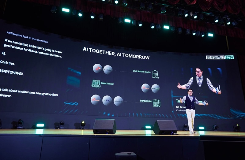 무대 위 대형 스크린에 “AI TOGETHER, AI TOMORROW”와 “SK AI SUMMIT 2024” 문구가 표시된 행사 현장. SK그룹 최태원 회장이 무대 중앙에서 손짓하며 프레젠테이션을 진행하고 있고, 스크린에는 ‘Green Fuel Cell’, ‘Small Modular Reactor’, ‘Energy Saving’ 등의 그래픽 다이어그램과 영어 및 한글 텍스트가 함께 보임.