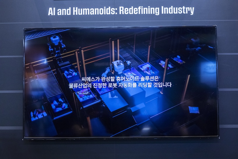 ‘AI and Humanoids: Redefining Industry’ 문구 아래 스크린에 로봇들이 물류 공정 라인을 자동화하는 영상이 재생되고 있다.