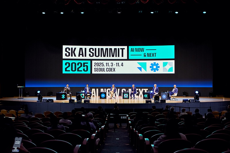 SK AI SUMMIT 2025 행사 전경. 무대에는 6명의 패널이 좌석에 앉아 있고 객석에는 관중들이 앉아 관람