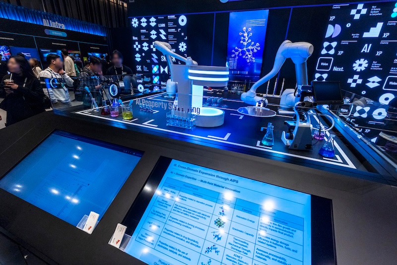 투명 아크릴 뒤 실험 테이블에 로봇 암과 시약 비커가 배치되어 있다. 하단 터치스크린엔 AI 기반 물성 예측 실험 워크플로우가 표시된다.