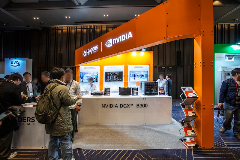 밝은 오렌지색 조형물 아래 NVIDIA 부스가 전시되어 있다. ‘NVIDIA DGX B300’ 문구와 함께 여러 참가자들이 설명을 듣고 있다.