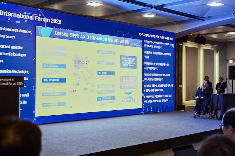 대형 스크린에 지역 산업 전반의 AX 대전환과 국가 균형 성장 전략을 설명하는 슬라이드가 표시되어 있다. 박태완 정책관이 무대 한쪽에서 내용을 발표 중이다.