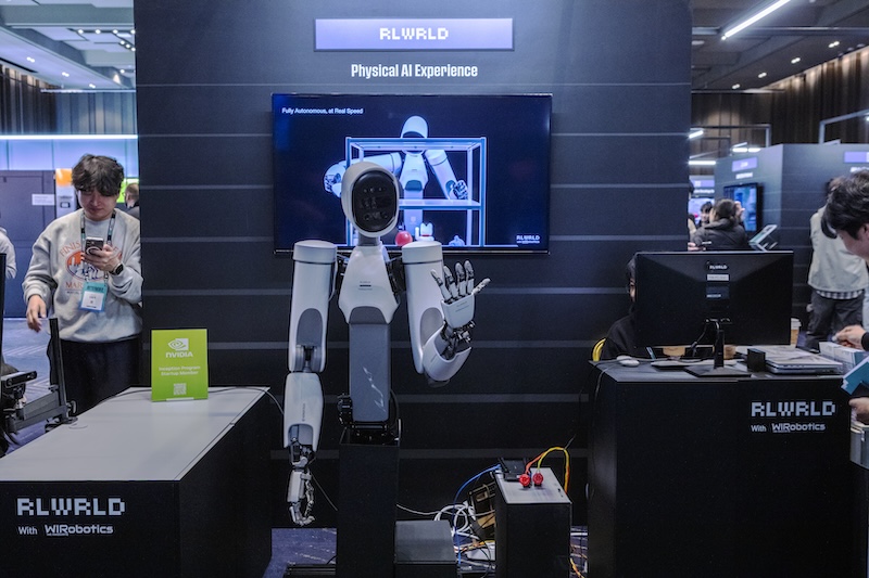 전시 부스 ‘RLWRLD Physical AI Experience’ 공간. 휴머노이드 로봇 ALLEX가 중앙에 서 있고, 뒤 스크린에는 ALLEX 작동 영상이 재생되고 있다.