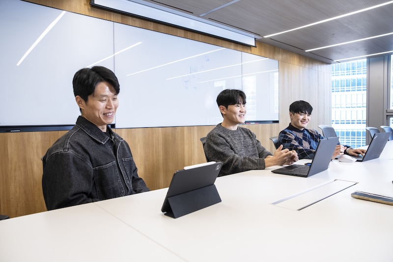 회의실 테이블에 앉은 오태석, 이경필, 정상민 님이 각자 노트북과 태블릿을 두고 웃으며 대화하는 모습.