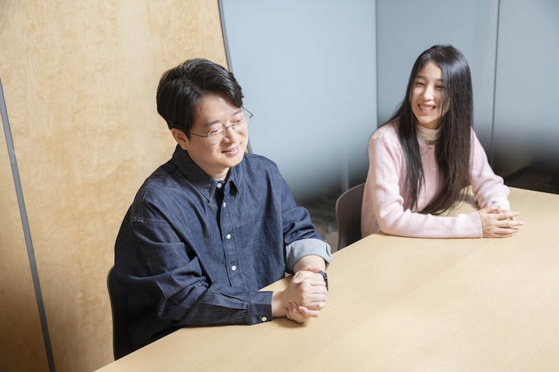 회의 중 미소를 짓는 천성준 님과 이유진 님. 두 사람이 테이블에 나란히 앉아 밝은 분위기로 대화하고 있다.