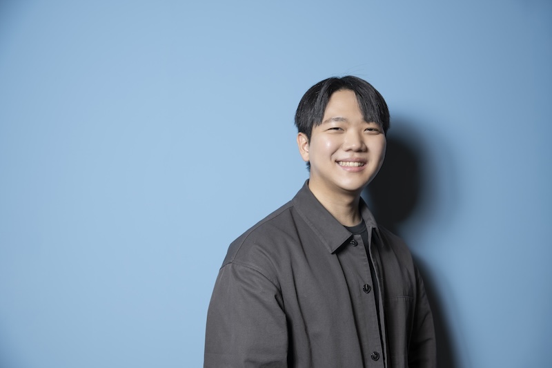 파란 배경 앞에서 웃으며 서 있는 양현호 님. 검은 셔츠를 입고 카메라를 바라보고 있다.