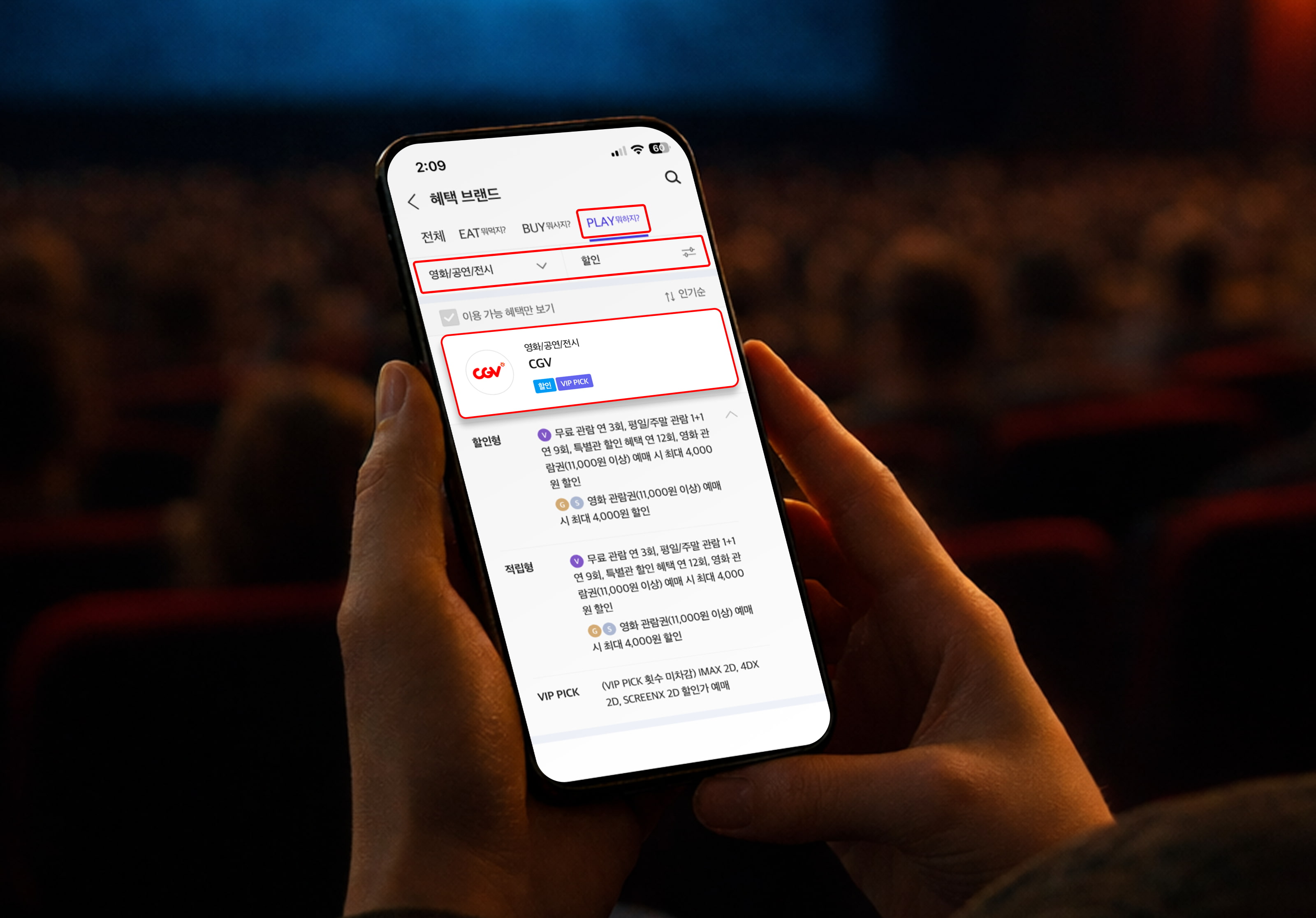 어두운 영화관 좌석 배경 속에서 스마트폰을 들고 있는 장면. 화면에는 ‘혜택 브랜드’ 메뉴의 PLAY 영역이 선택되어 있으며 ‘CGV’ 영화관 혜택과 VIP PICK 관련 할인 정보가 표시되어 있어 T멤버십 영화 관람 혜택을 확인하는 모습이 표현되어 있다.