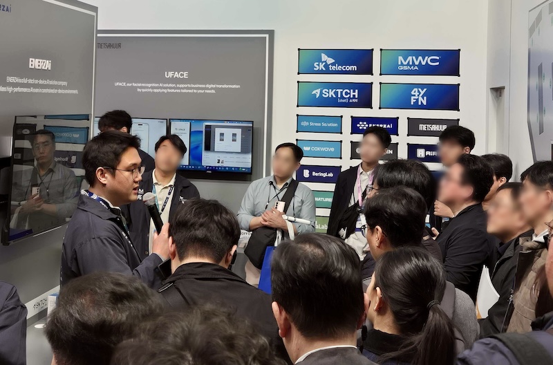 MWC26 4YFN SKT SKTCH 전시관에서 에너자이(ENERZAi) 장한힘 대표가 UFACE 얼굴인식 AI 솔루션을 소개하고 있다. 뒤편 스크린에 SK telecom, MWC GSMA, SKTCH, 4YFN, Stress Solution, ENERZAi 등 참여 기업 로고가 보인다.
